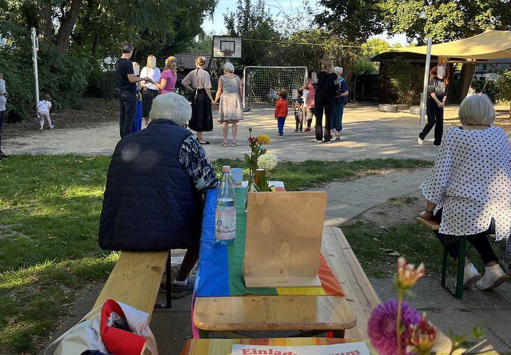 Kinder und Erwachsene im Garten der Kita Albatros sitzen an Tischen oder stehen auf dem Bolzplatz